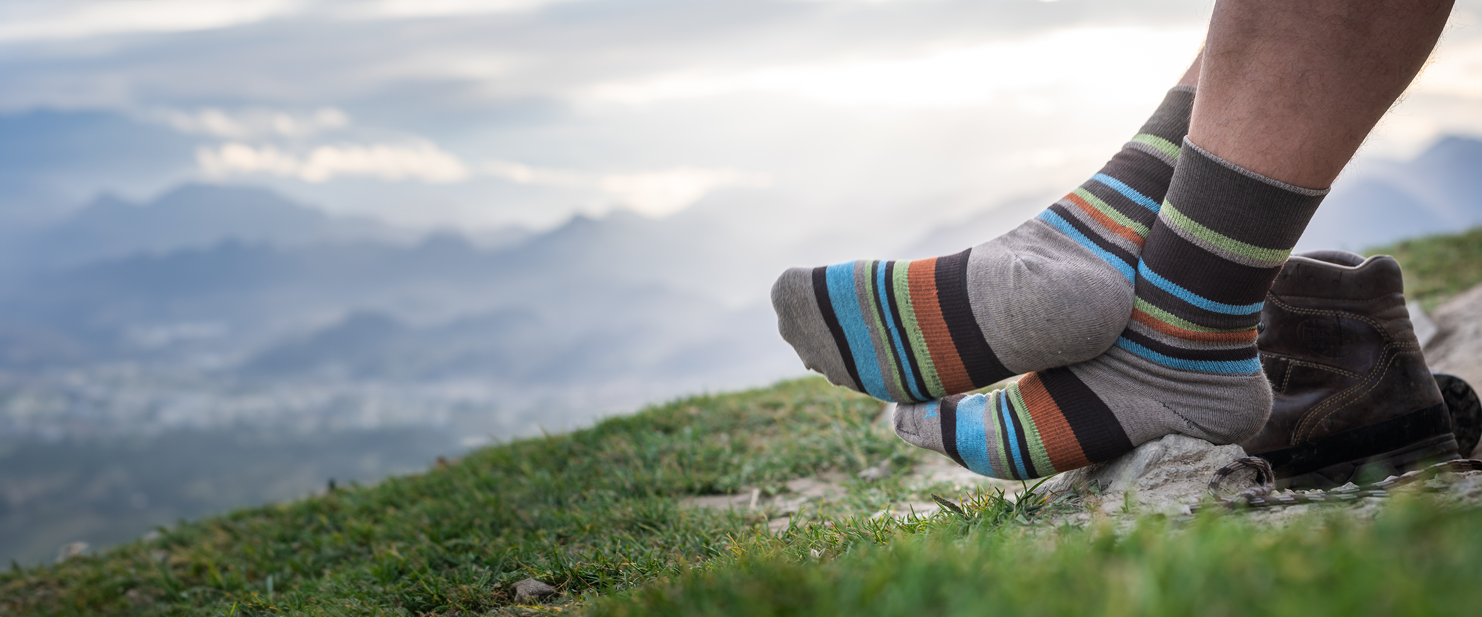 Gestreifte Wandersocken Stride Crew von Wrightsock vor Bergkulisse.